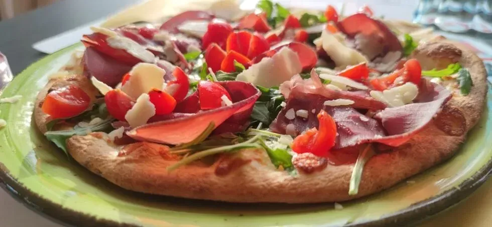 Pizza con condimenti: pomodori, carne, formaggio e verdure su un piatto verde.