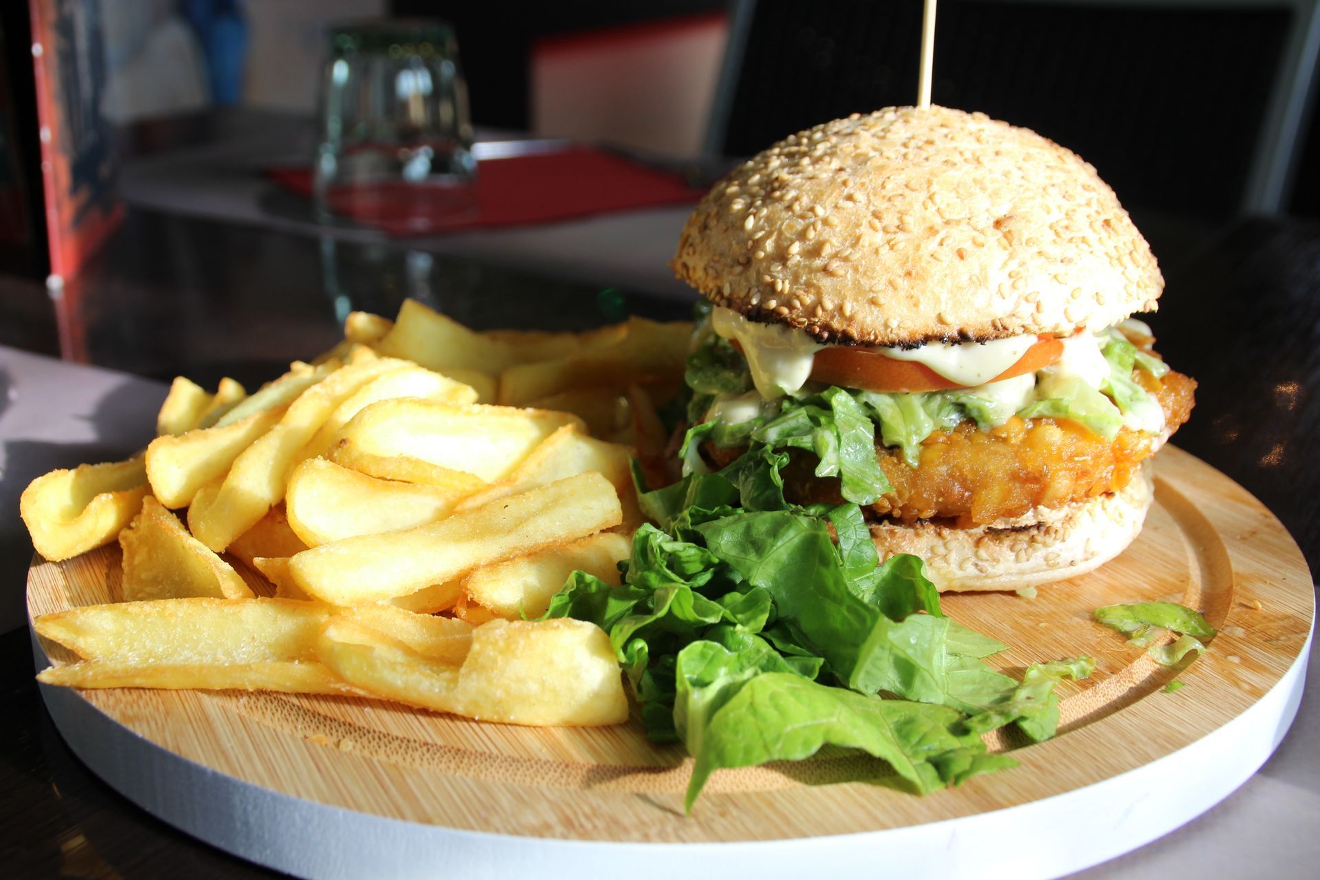 Hamburger con patatine fritte su un piatto di legno. L'hamburger è fatto con panino al sesamo, lattuga, pomodoro e salsa.
