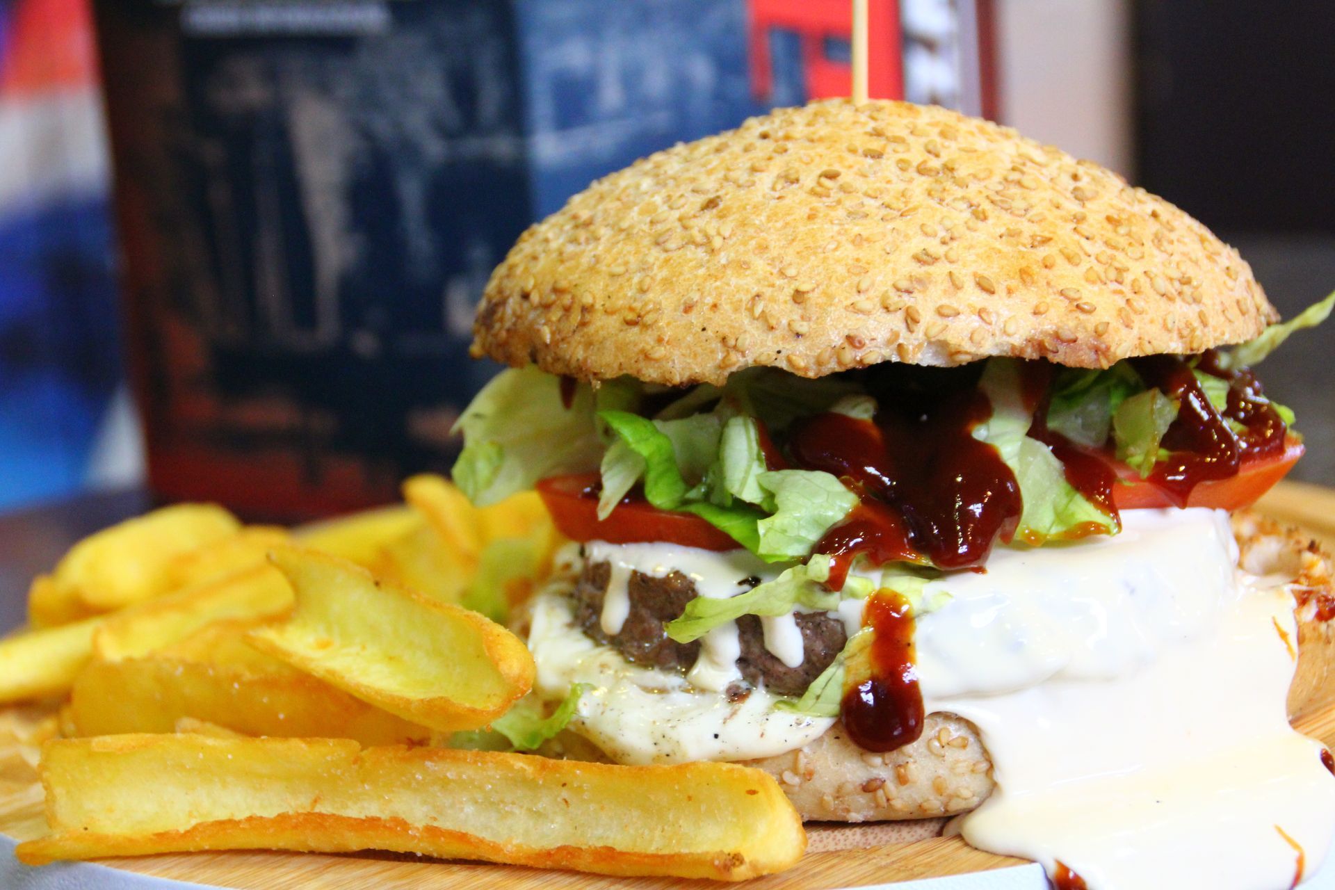 Hamburger con lattuga, pomodoro, salsa e patatine fritte su un tagliere di legno.
