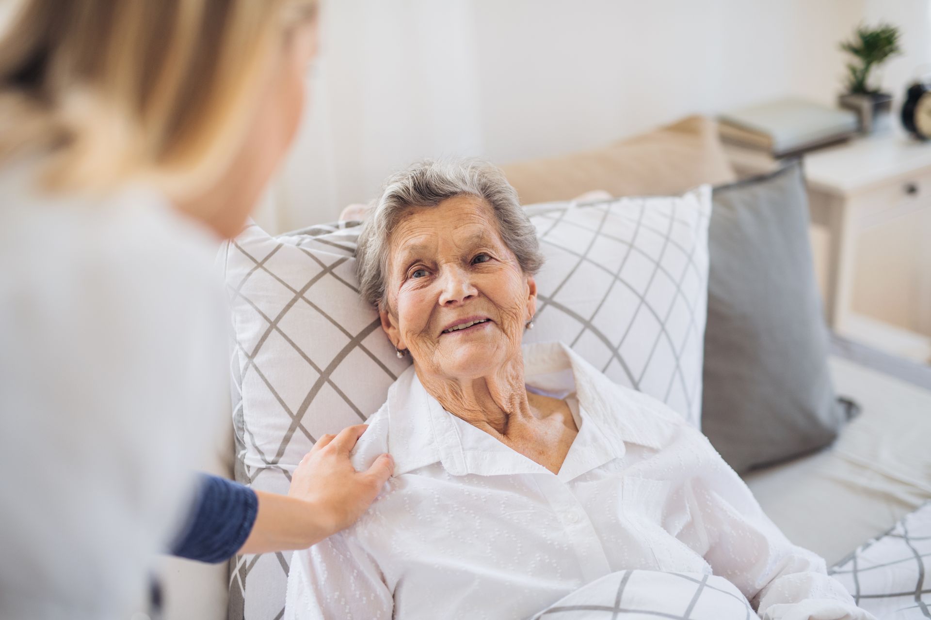 Woman in bed smiles at person touching her shoulder.