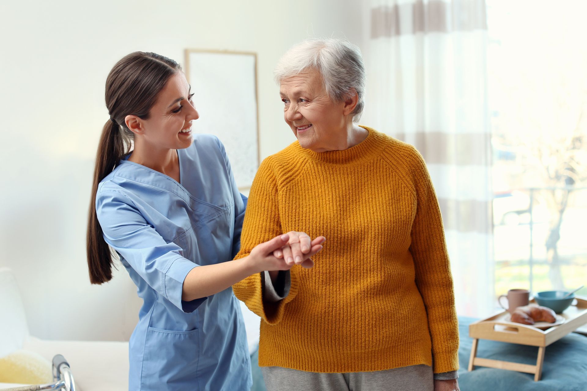 Caregiver assists an older person in walking. Both smile in a bright room.