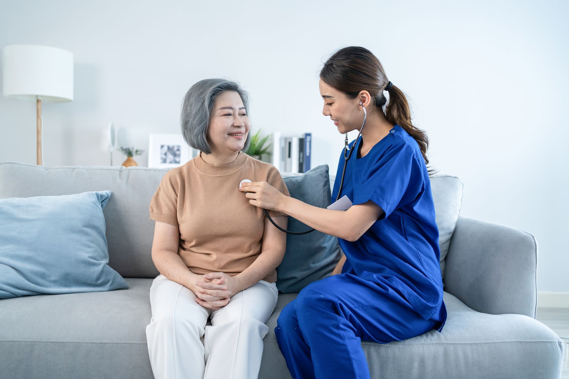 Nurse using a stethoscope on a patient sitting on a couch in a home setting.