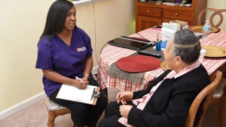 A person in scrubs interviews another person seated at a table.
