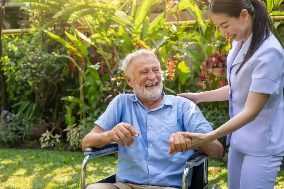 Man in wheelchair smiling with healthcare worker in garden.