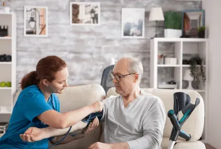 Nurse taking a patient's blood pressure at home, using a stethoscope and cuff.