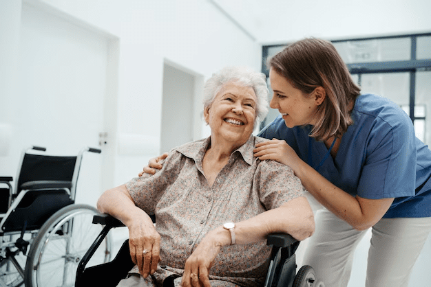 Woman in wheelchair smiles at caregiver in hallway, arms around shoulders.