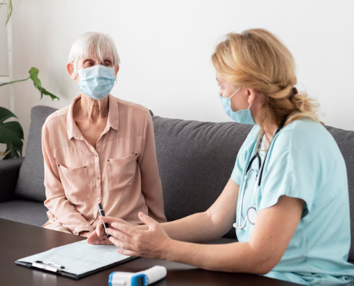 Elderly patient consults with medical professional, both wearing masks, at home.