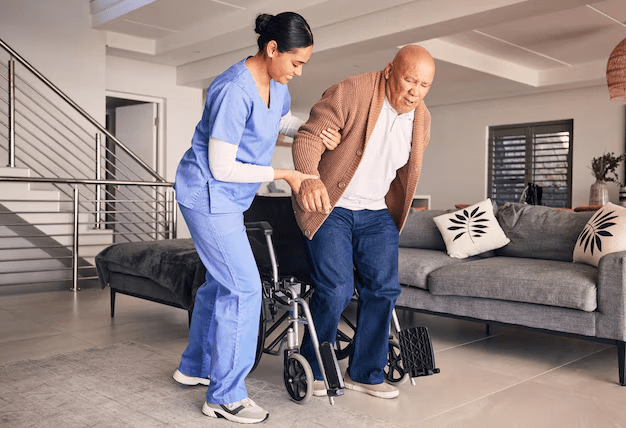 Caregiver assisting a person out of a wheelchair in a living room.