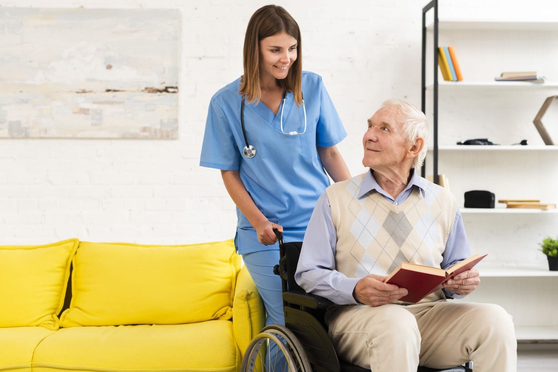 Nurse in blue scrubs assists elderly man in wheelchair.