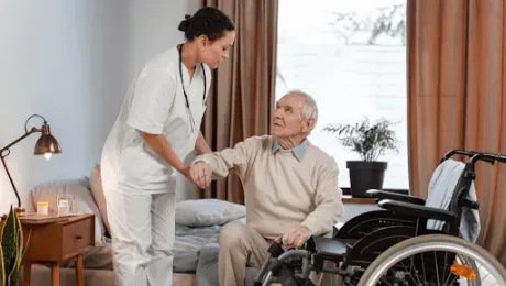 Caregiver assisting a person in a wheelchair indoors.
