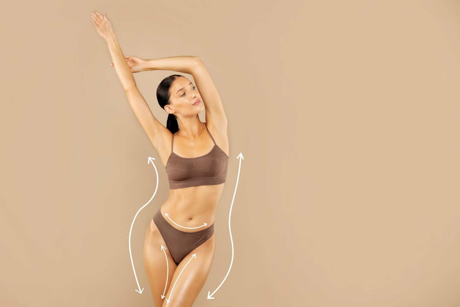 Woman in brown activewear posing with raised arms against a beige background.