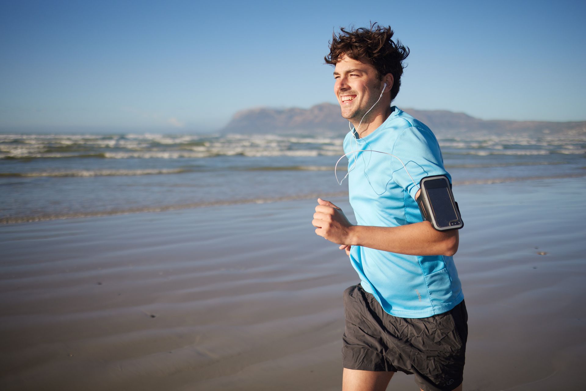 A man is running on the beach with headphones on.