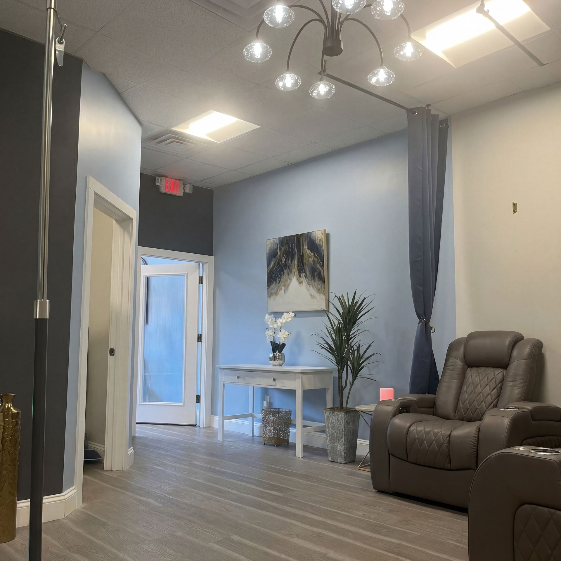 A quiet room with light blue walls, a white side table, a potted plant, and a brown leather reclining chair.