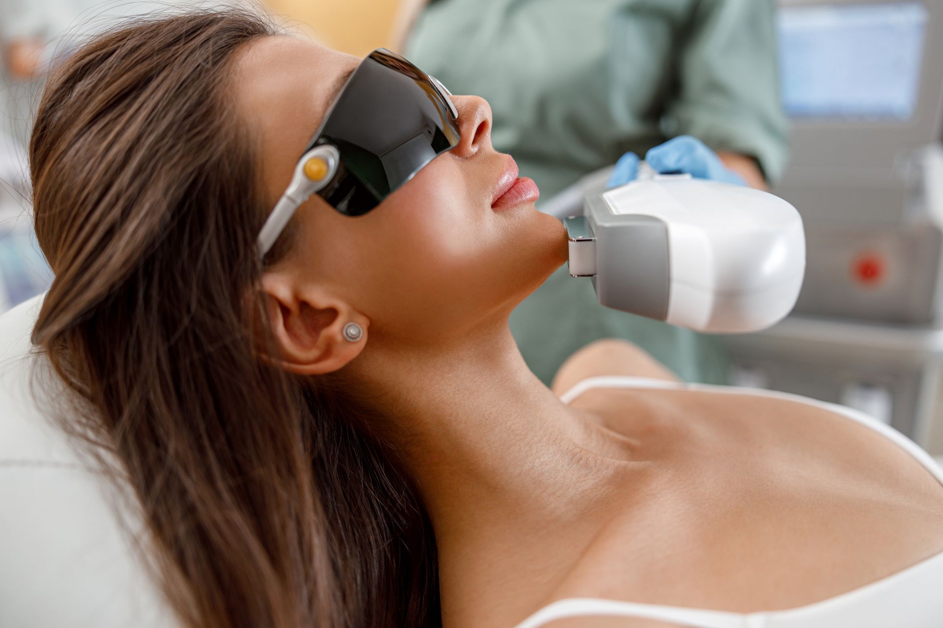 Woman receiving laser treatment on her face, wearing protective eyewear in a medical setting.