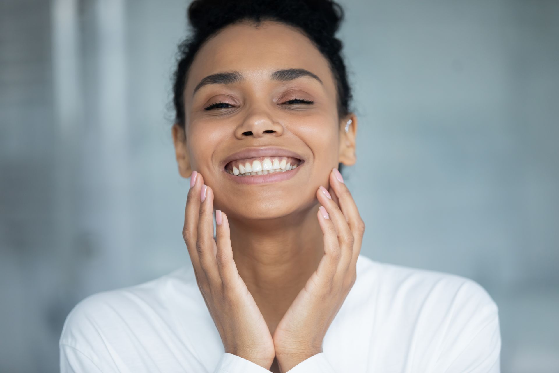 A woman is smiling and touching her face with her hands.