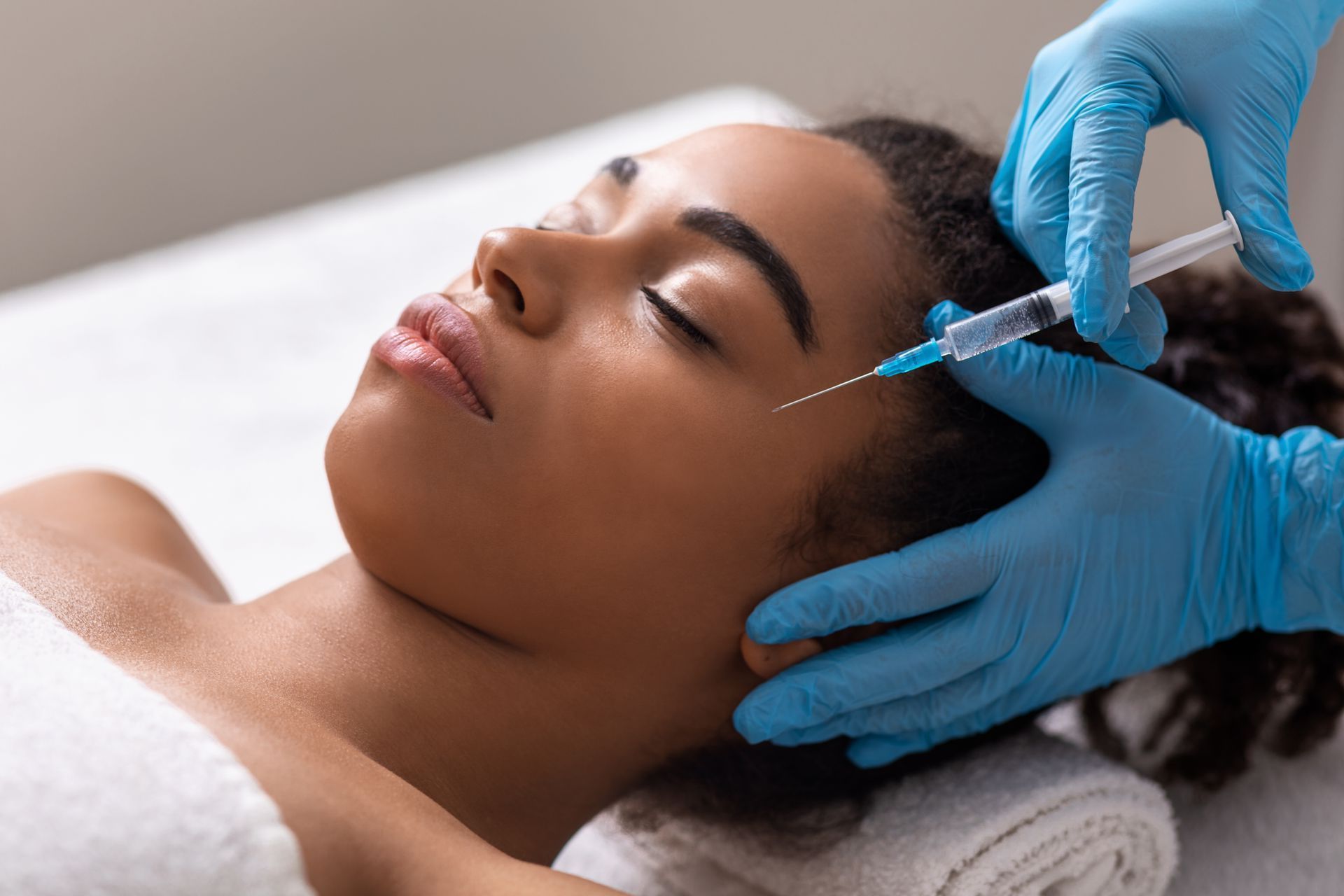 A woman is getting a botox injection in her forehead.