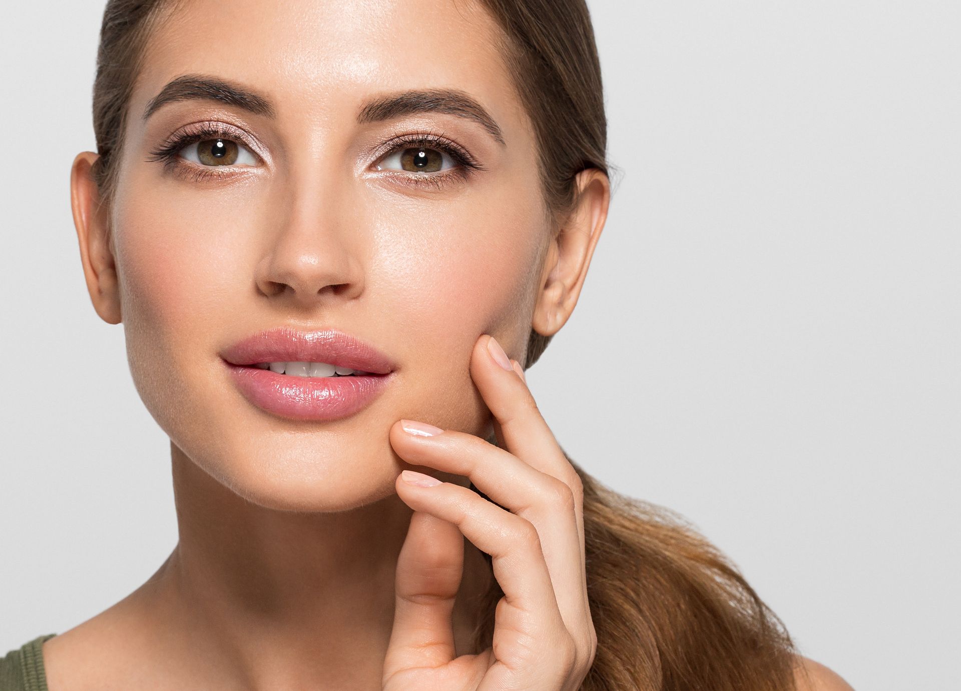 A person with a neutral expression touching their cheek, set against a plain grey background.