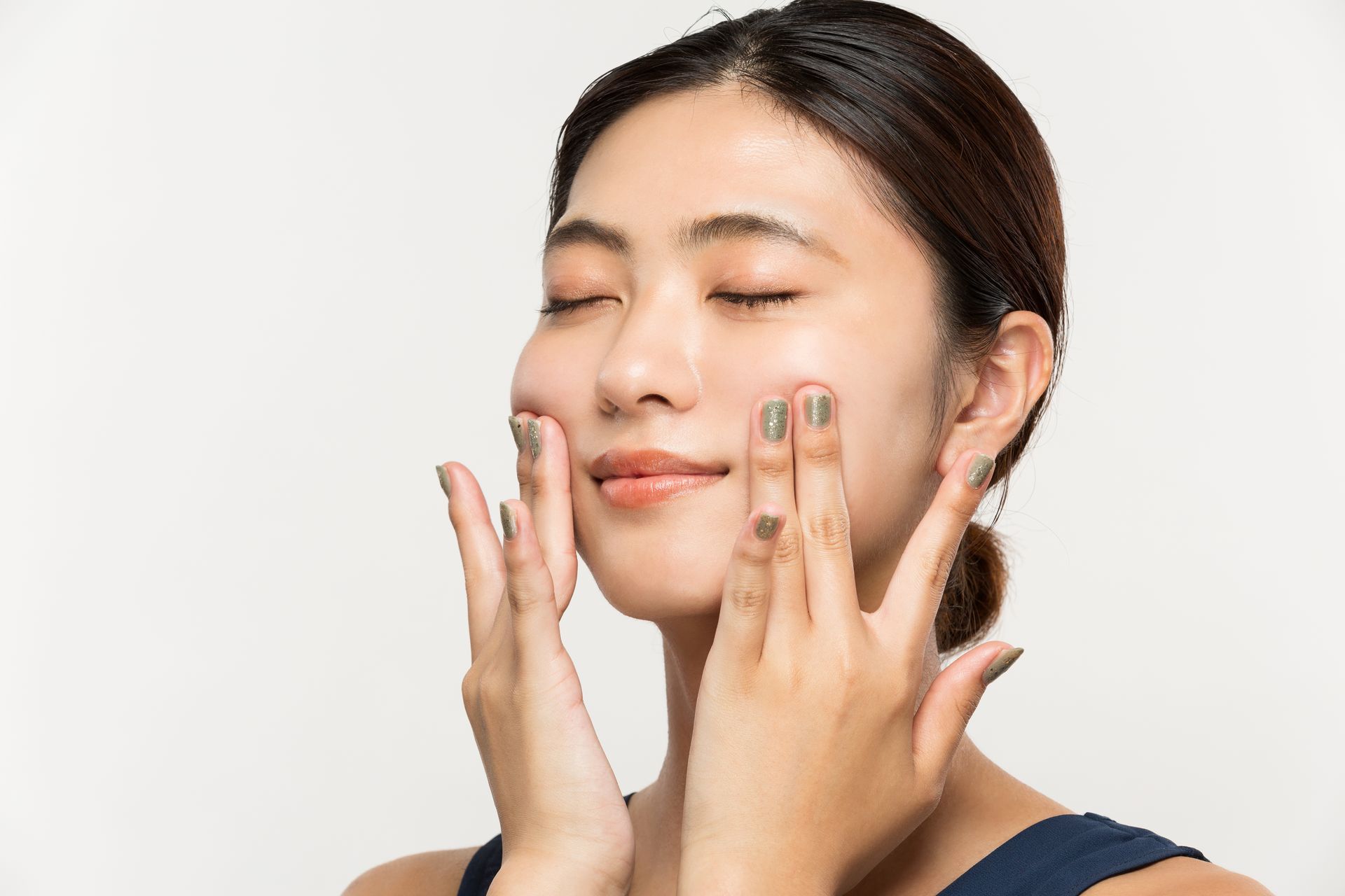 A woman is applying lotion to her face with her hands.
