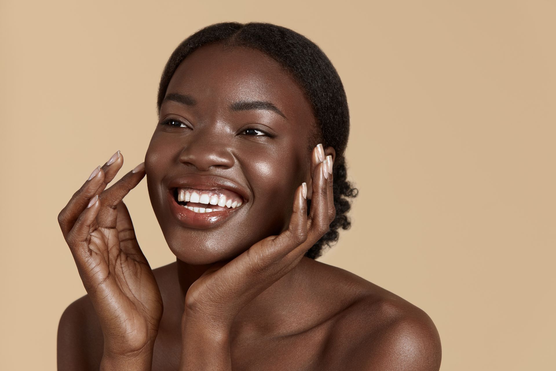 A woman is smiling and touching her face with her hands.