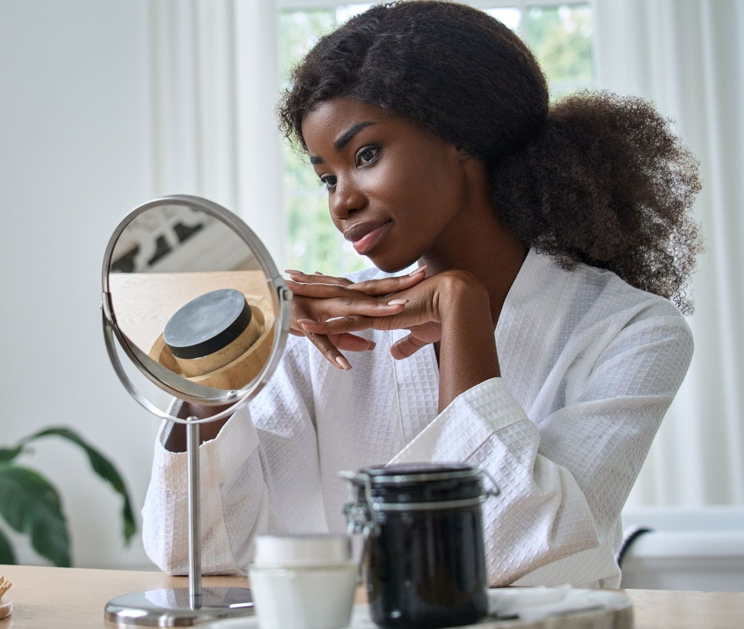 A woman is looking at her face in a mirror.