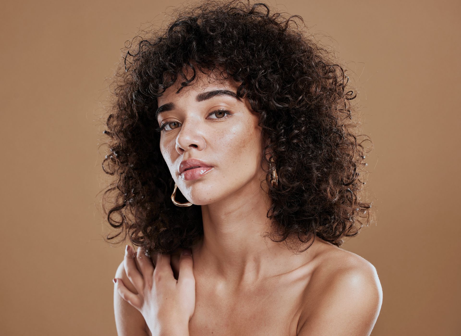 A woman with curly hair and hoop earrings is looking at the camera.