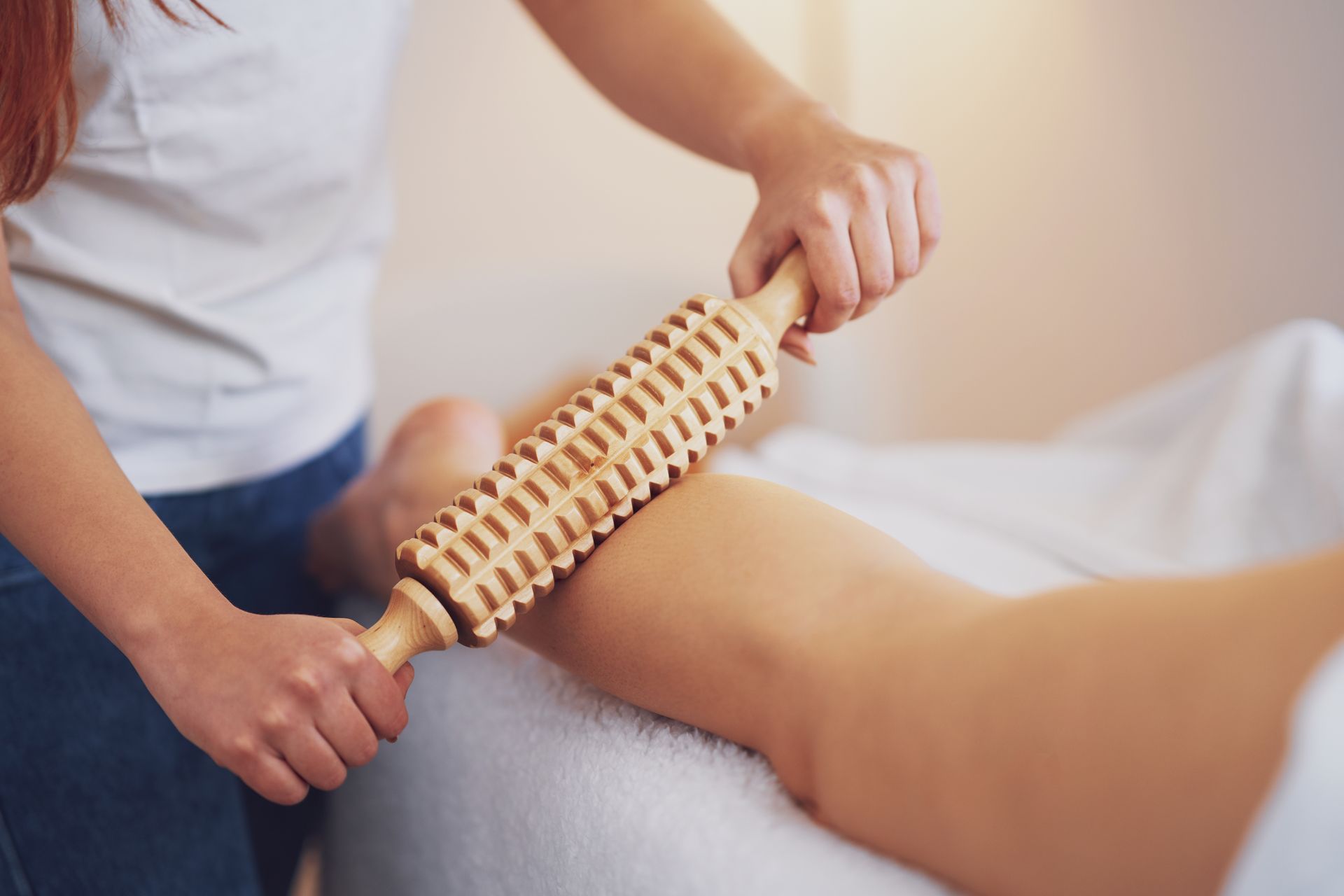 A woman is giving a leg massage with a wooden roller.