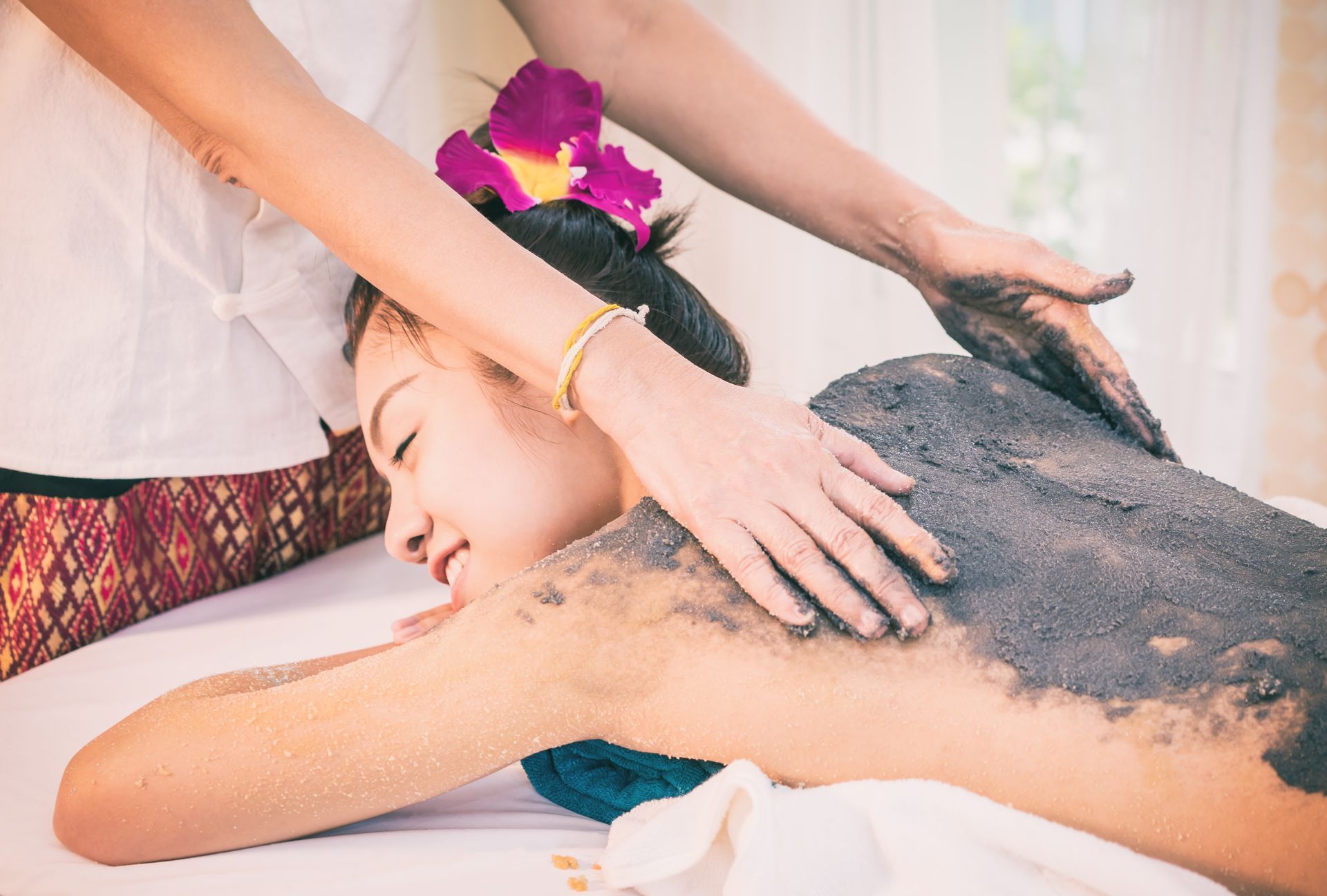 A woman is getting a massage with black mud on her back.