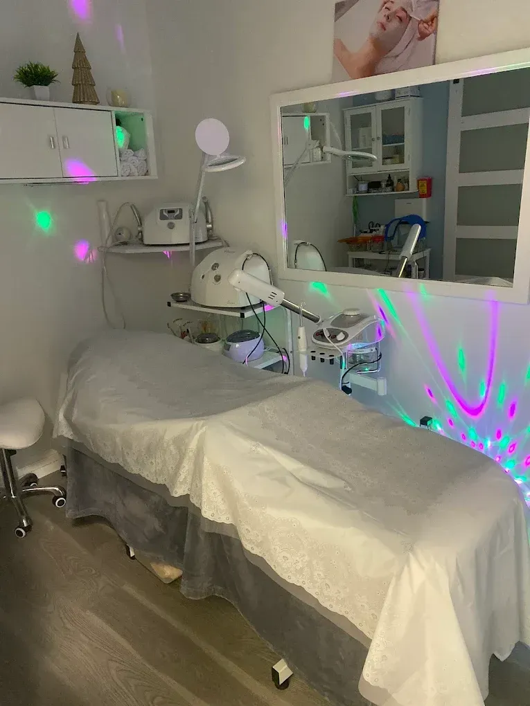 A spa treatment room featuring a massage table, specialized equipment, a large mirror, and colorful decorative lighting.