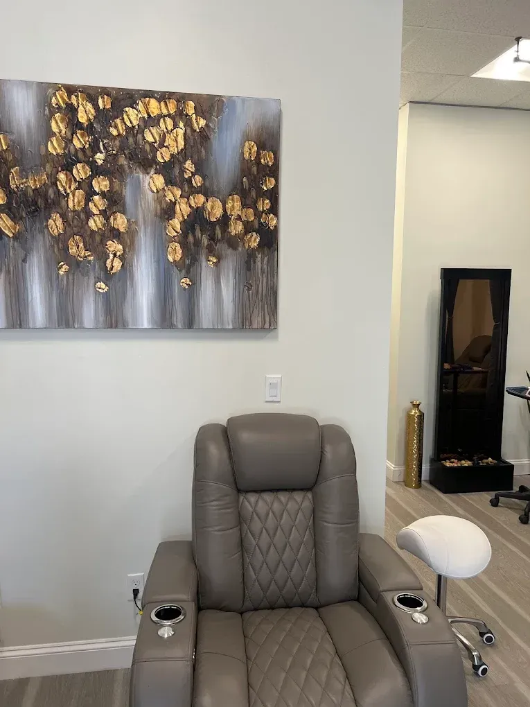 A grey, diamond-tufted reclining salon chair with cup holders sits before a large abstract gold and grey wall painting.