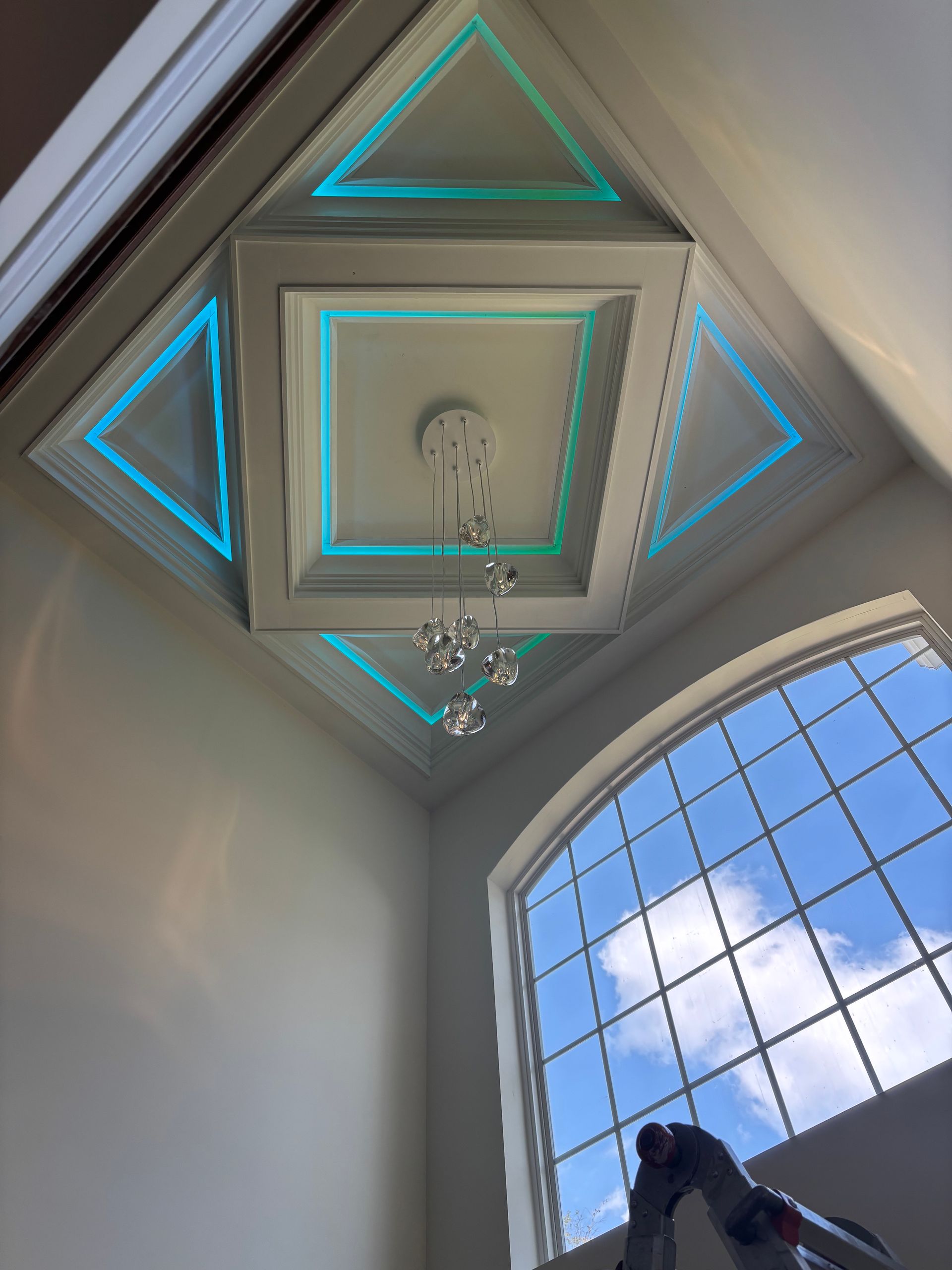 Electrician in a white hard hat installs an outlet using a drill on a white wall.