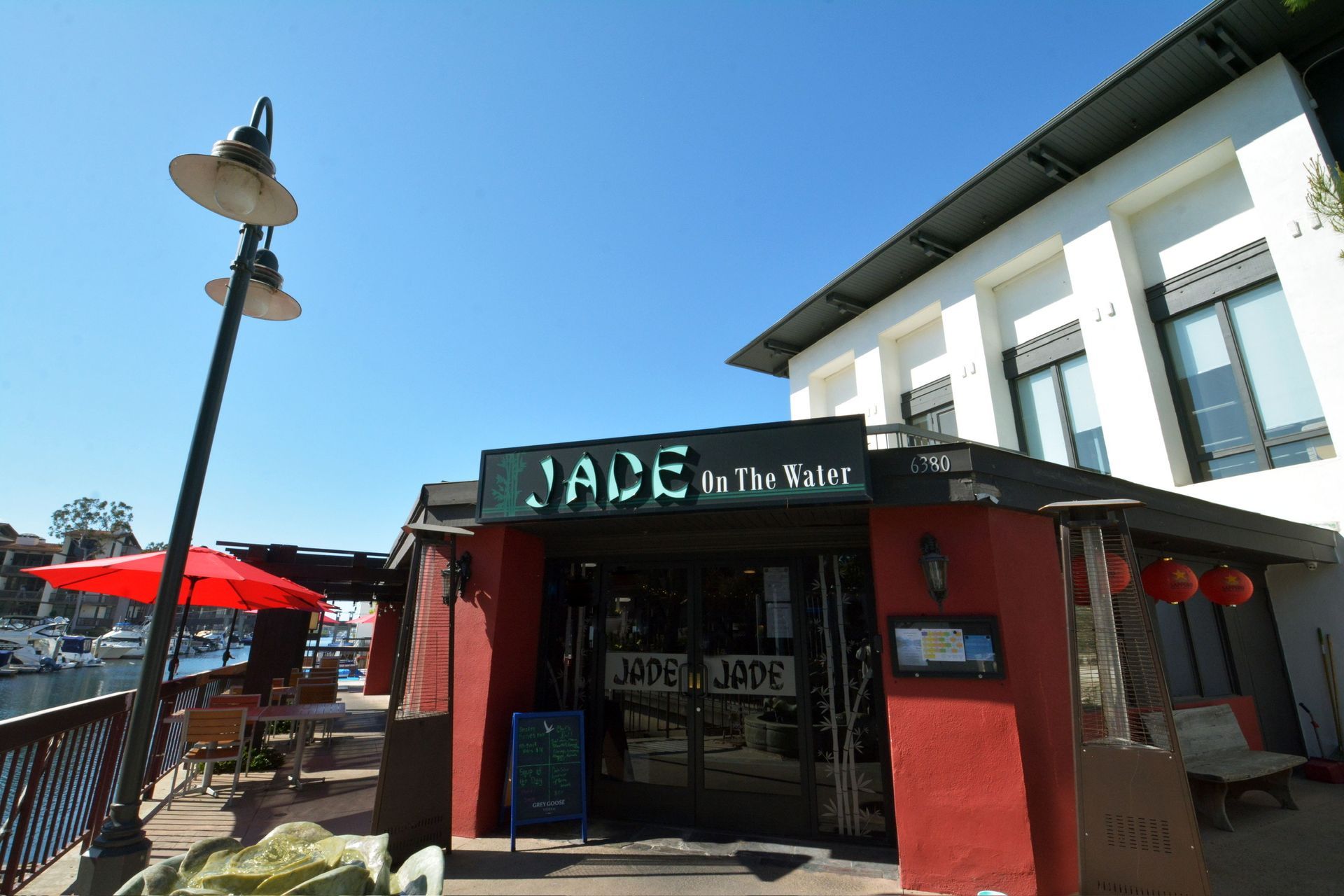 Outdoor café storefront with red umbrellas and a green sign on a sunny street corner