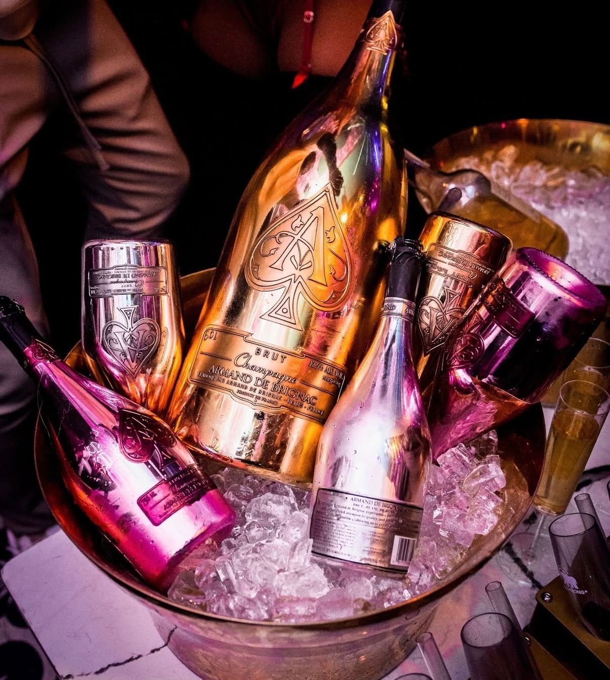 Bottles of champagne in an ice-filled bucket, lit with pink and gold reflections.