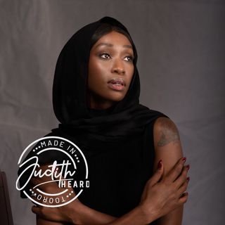 Woman in black hooded top posing against a gray backdrop, looking off to the side.