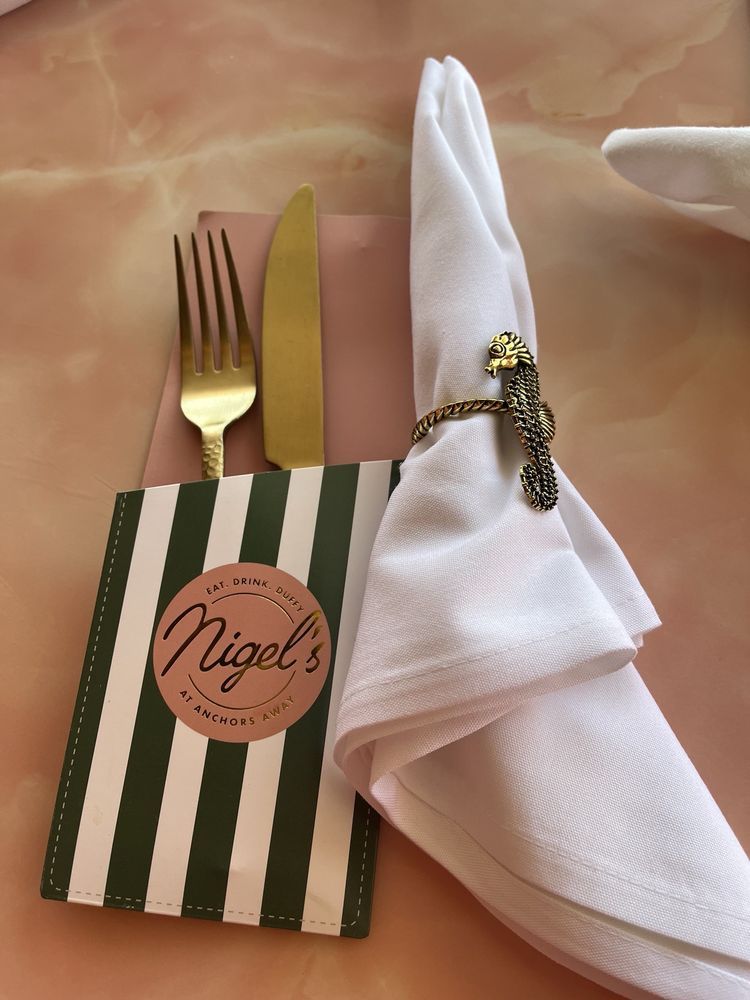 Gold silverware in a striped holder beside a white napkin with an ornate ring on a peach tablecloth
