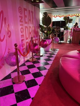 Pink-lit lounge with checkered floor, velvet stanchions, and a neon drink sign