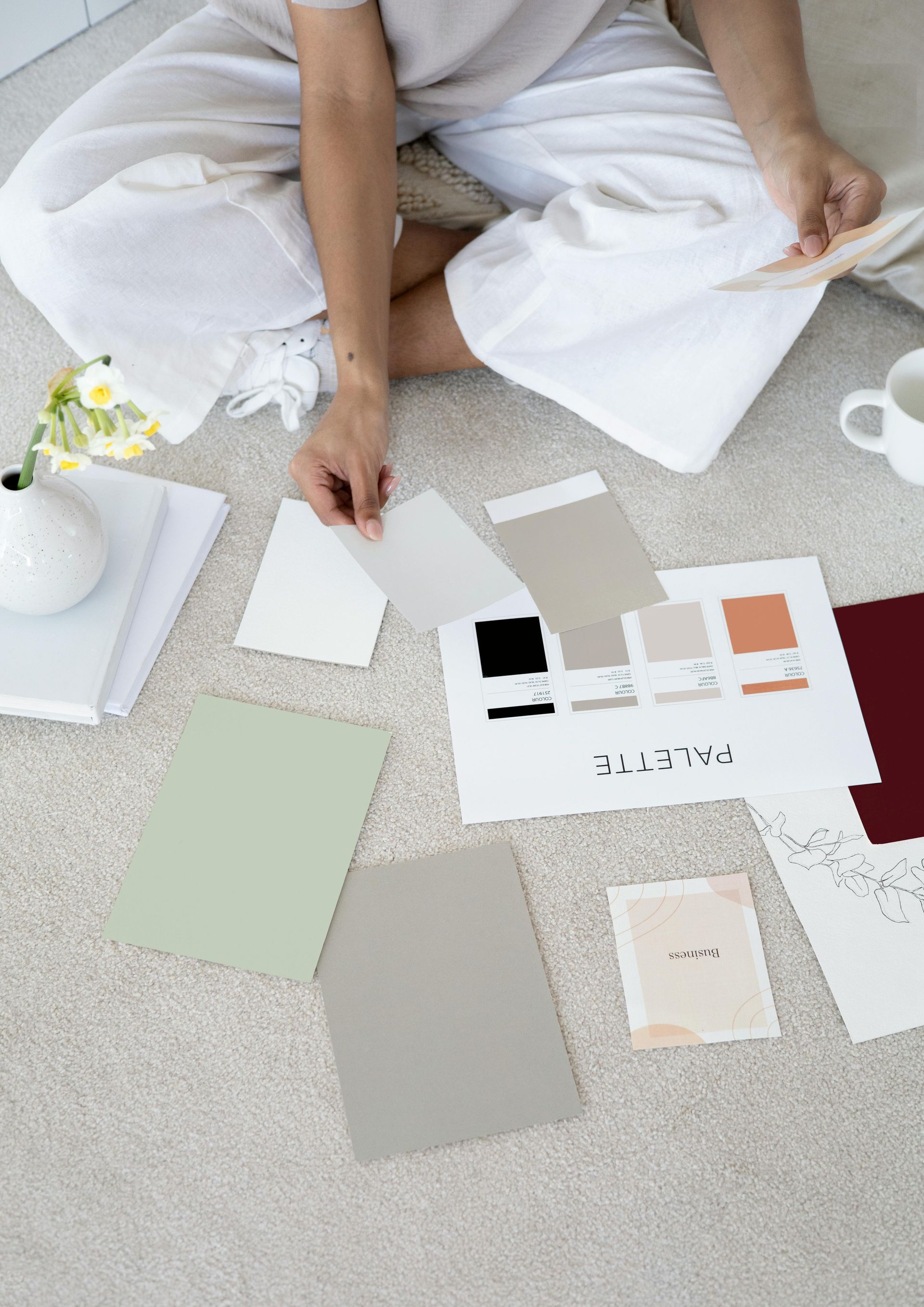 Person on floor looking at paint swatches on a carpet.