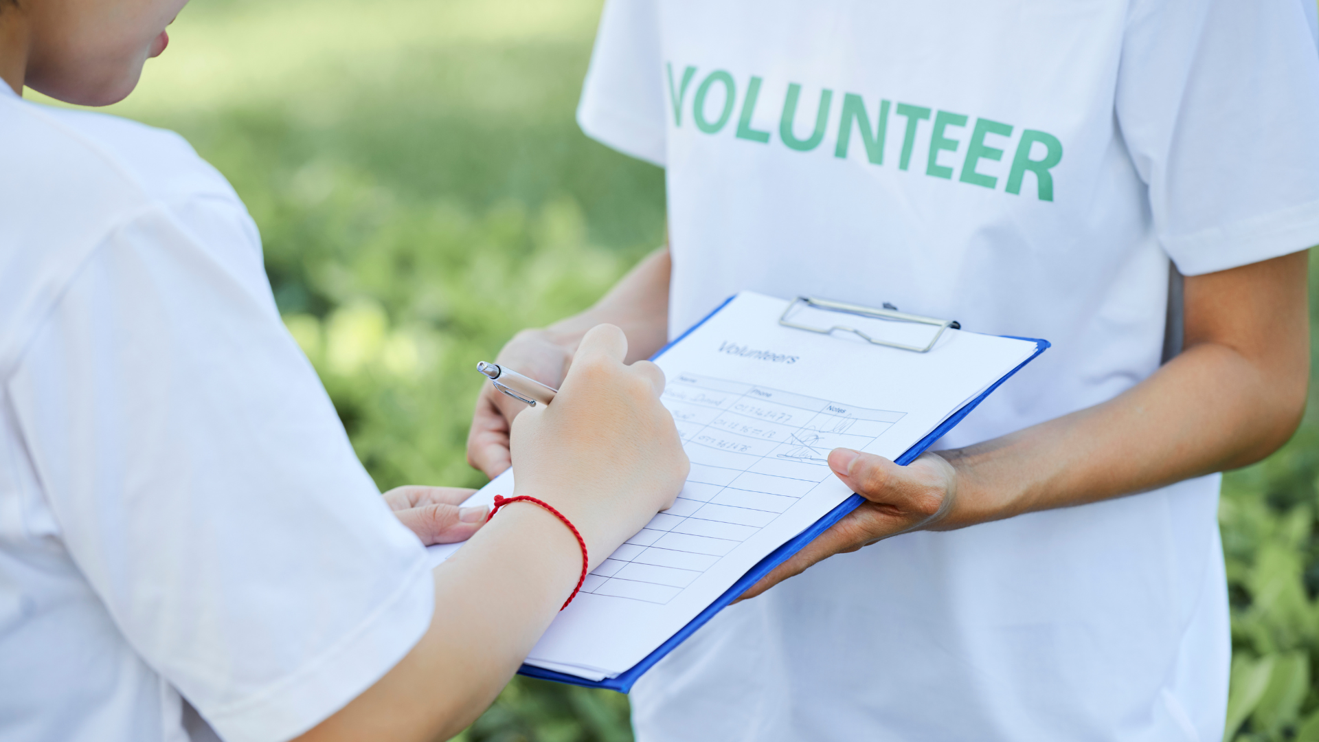 Person signing a form on a clipboard held by a volunteer wearing a white shirt with