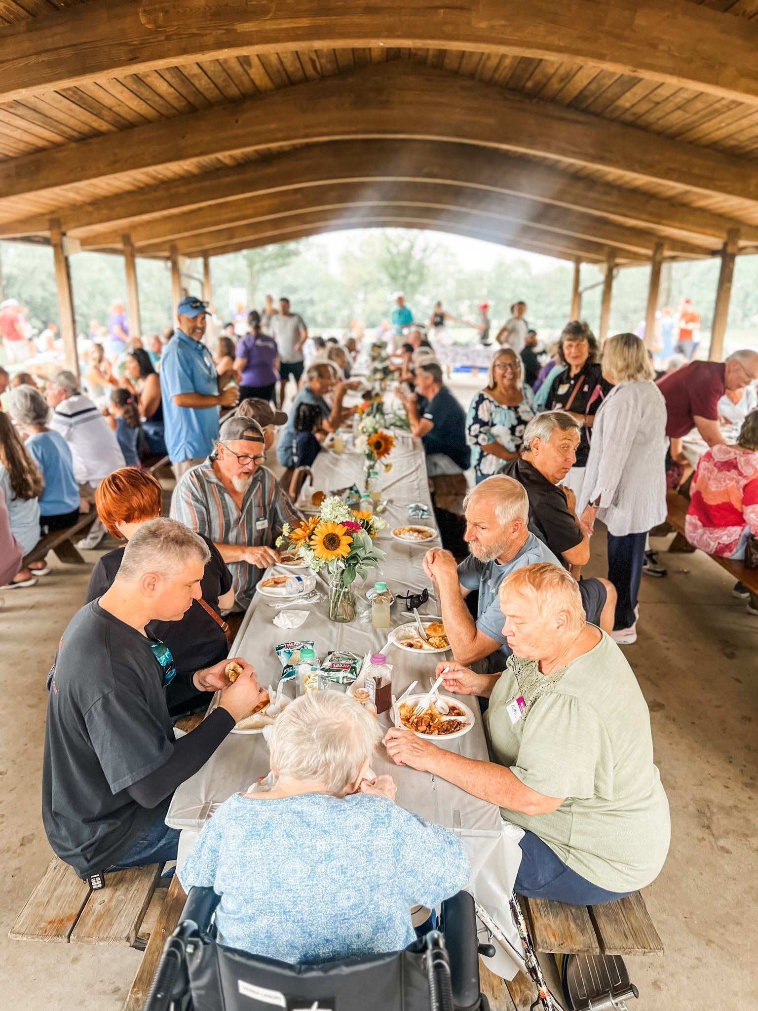 People seated at a long table in a covered outdoor area, enjoying a meal and socializing.