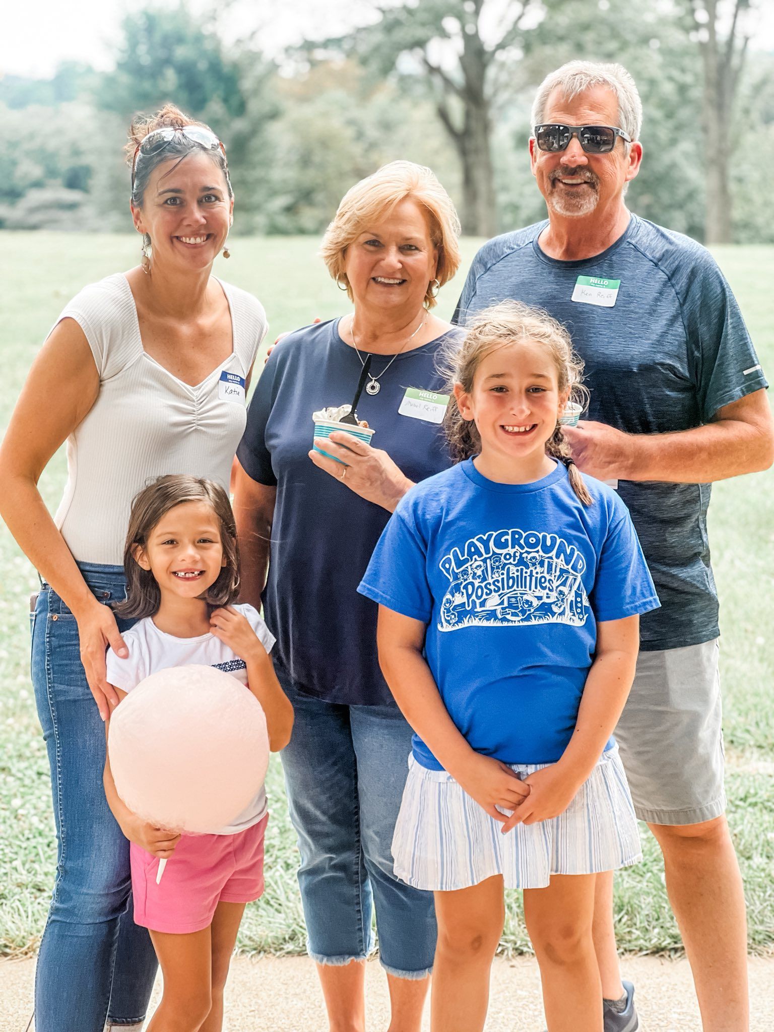 Family group poses outdoors; two young girls hold a balloon, smiles.