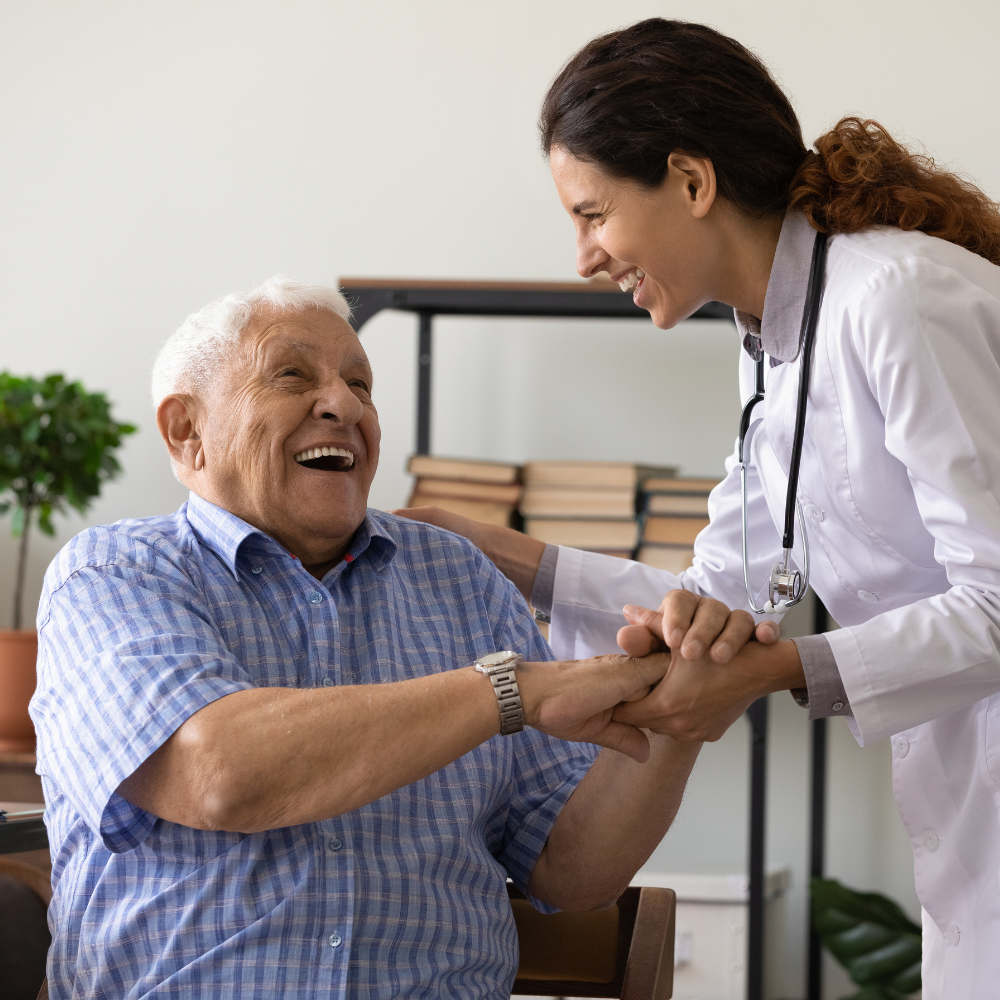 A doctor in a white coat smiles, holding hands with a smiling older person in a blue shirt.