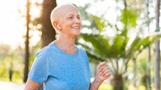 Woman with a shaved head smiles while jogging outdoors; wearing a blue shirt and earbuds.