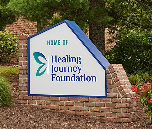 Sign for Healing Journey Foundation; white with blue trim, brick base, green logo.