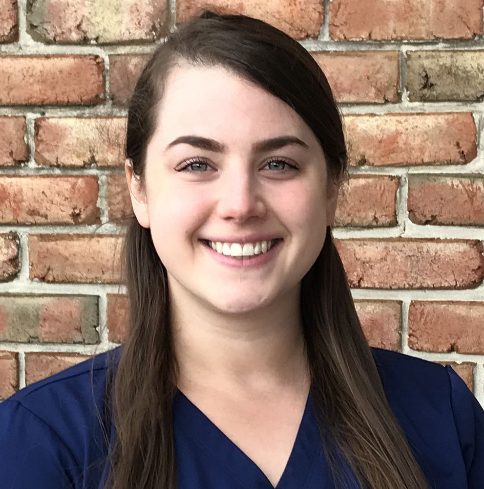 HJF Board of Directors | Woman with dark hair smiling in front of a brick wall, wearing a blue scrub top.