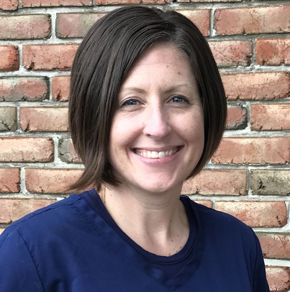 Melissa Leaman for Healing Journey Foundation | Woman with short brown hair smiling, wearing a navy shirt, in front of a brick wall.
