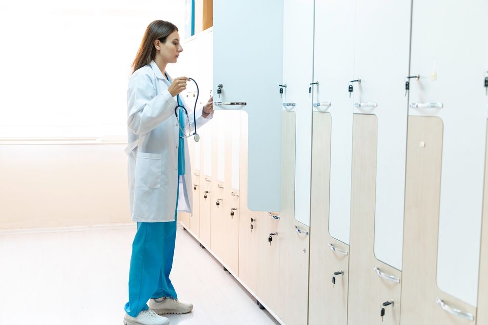 A female doctor is standing in a locker room holding a stethoscope.