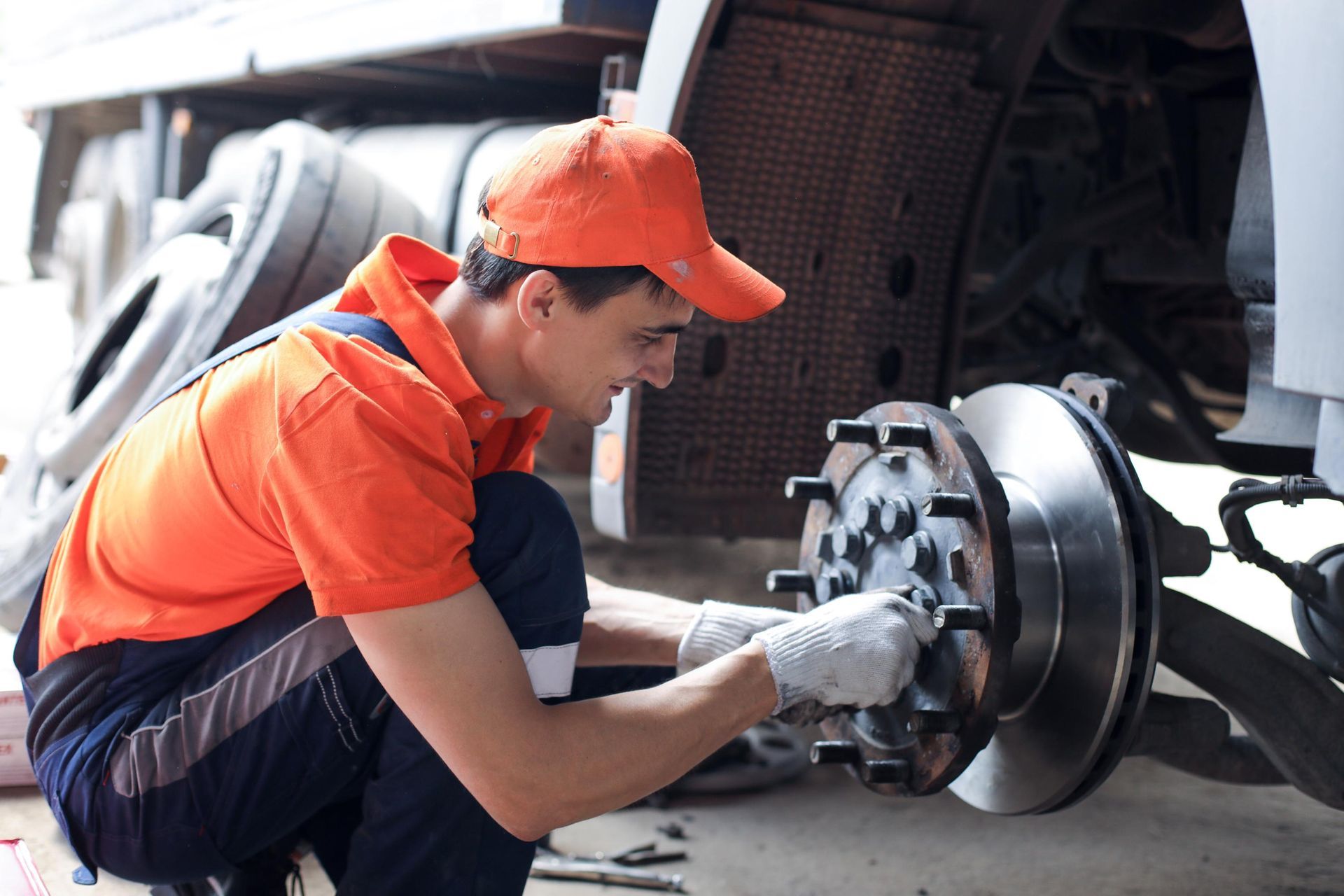 Mechanic in orange uniform working on a car brake assembly in a garage