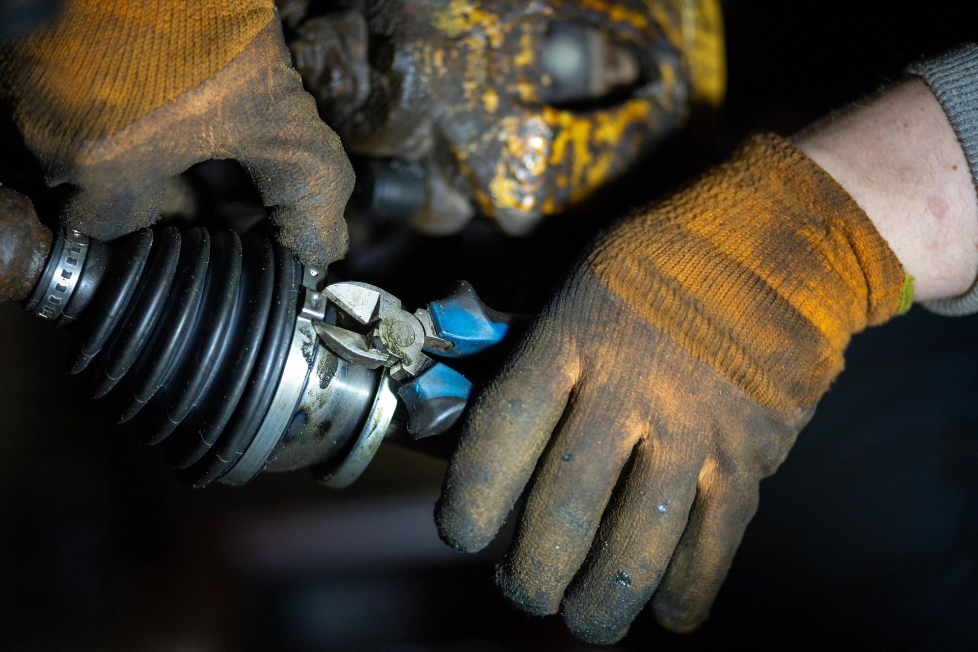 Gloved hands working on a dirty metal joint with a rubber boot in a dim workshop