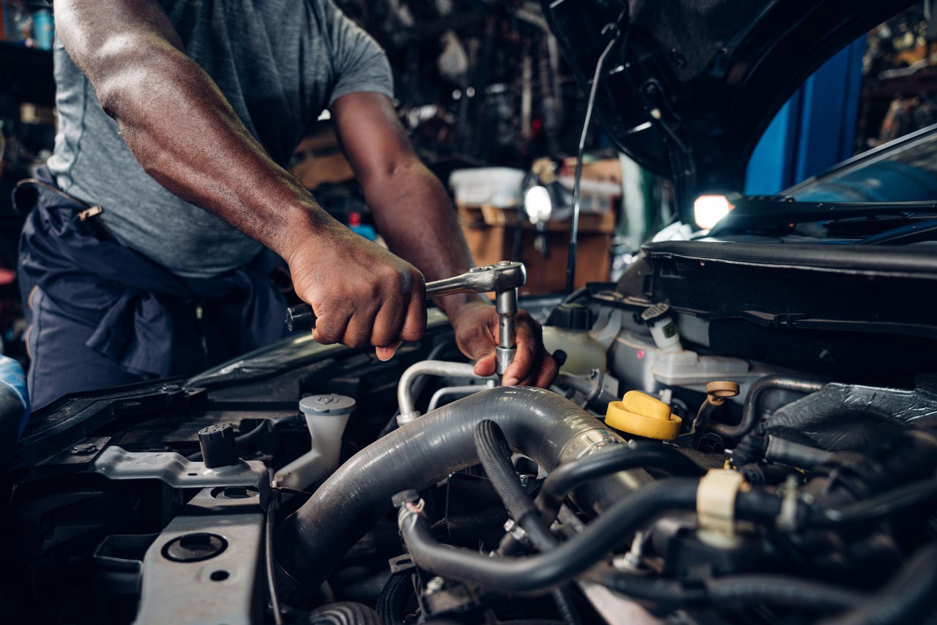 Mechanic working under a car hood with tools in an auto repair shop