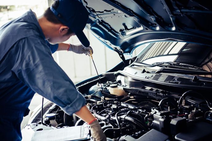 Mechanic using tools to inspect a car engine under an open hood
