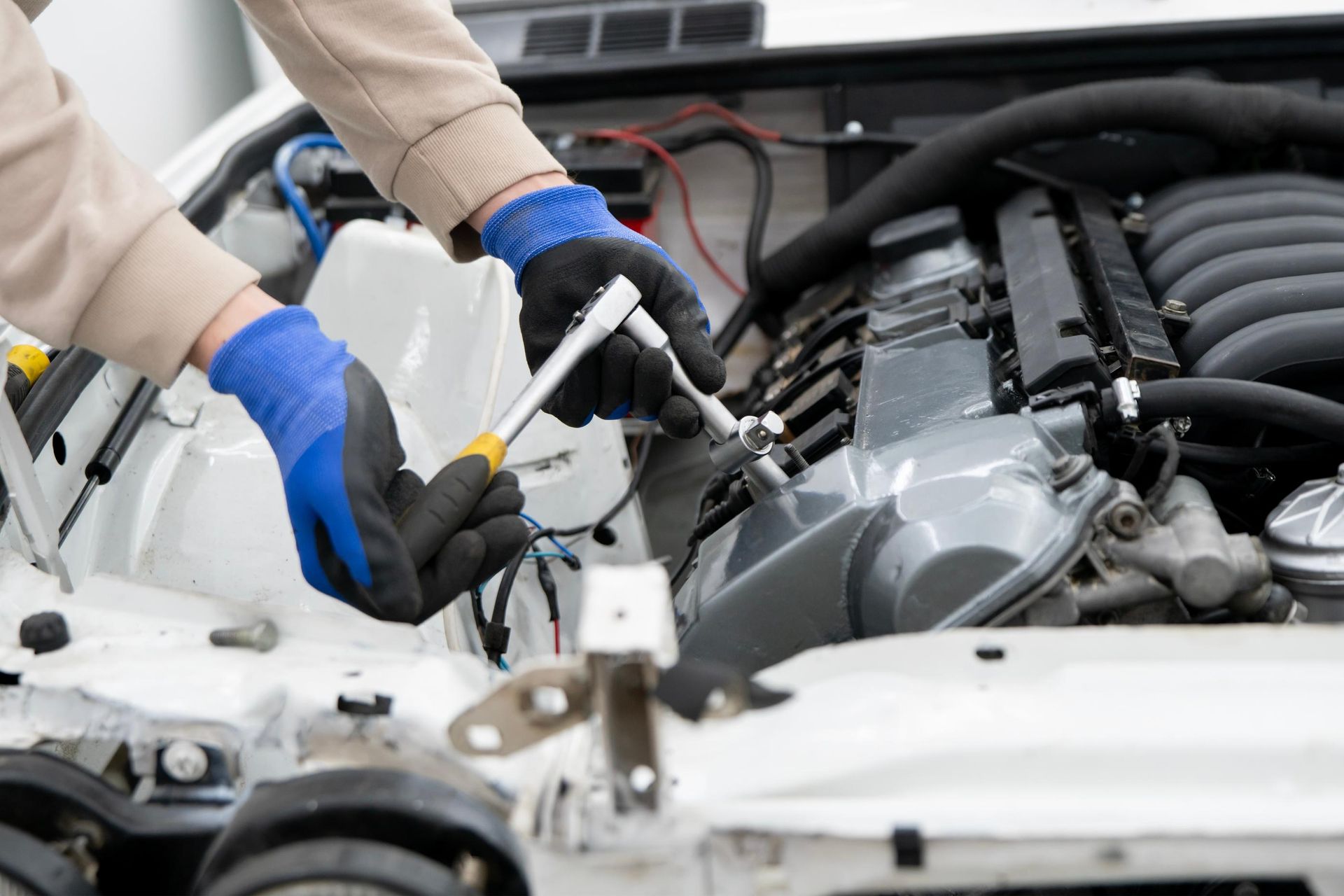 Mechanic wearing blue gloves working on an open car engine in a repair shop